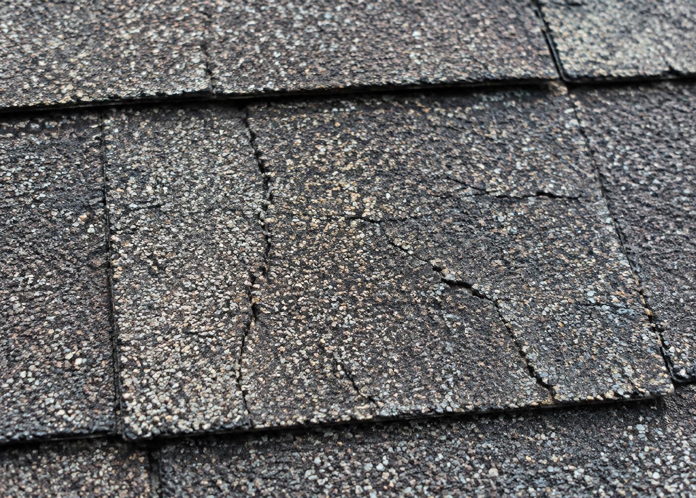 Dry asphalt shingles with visible cracks and brittle surface wear